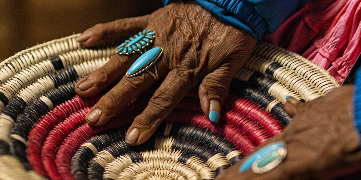 An Elderly Native American Woman (Navajo) Wearing Turquoise Rings on Her Fingers Touches a Woven Navajo Basket